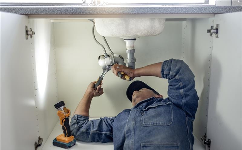 Plumber repairing pipes beneath a bathroom sink in Merritt Island