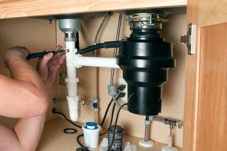 Plumber installing a garbage disposal beneath a kitchen sink in Merritt Island