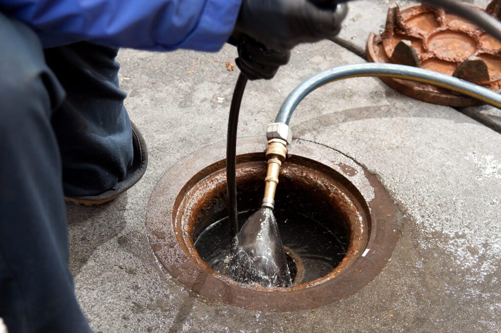 Plumber hydro jetting a sewer line through a manhole in Merritt Island