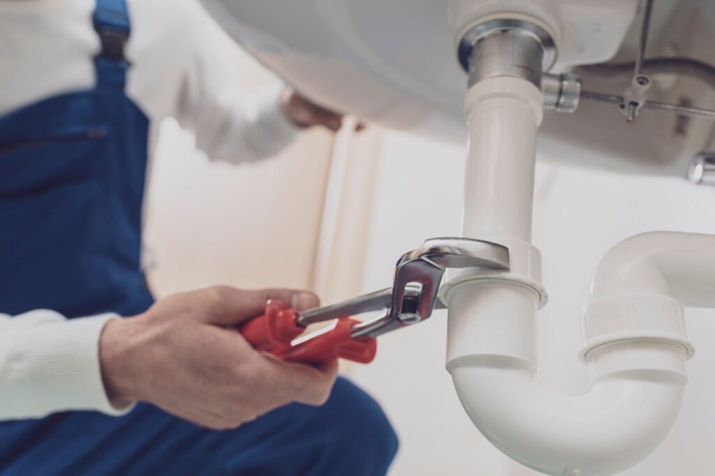 Plumber repairing a white drain pipe beneath a sink in Merritt Island