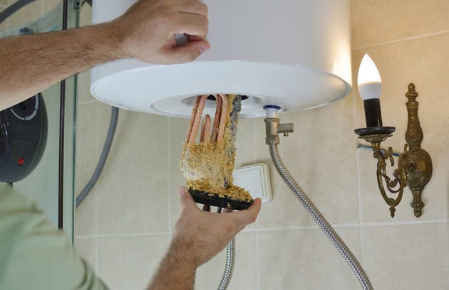 Technician removing mineral buildup from a water heater in Merritt Island